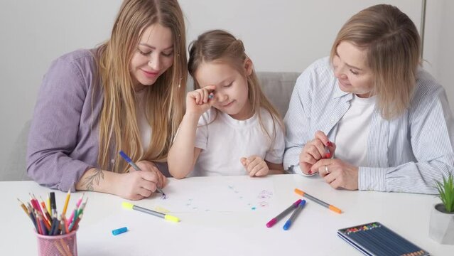 Creative family. Art therapy. Female relationship. Cute little girl enjoying drawing with mother and grandmother with colorful markers in light room interior.