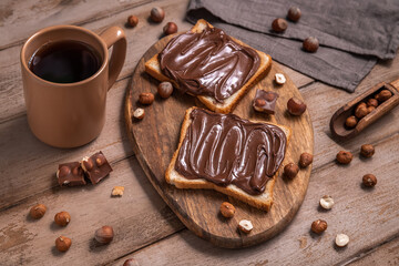 Board of bread with chocolate paste and hazelnuts on wooden background