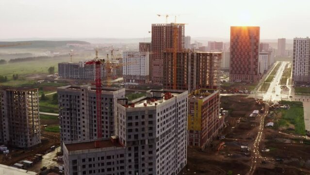 Construction of new microdistrict with multistorey buildings taken by drone. Top, above view of urban area with unfinished highrise blocks, apartment houses, cranes, moving cars on roads