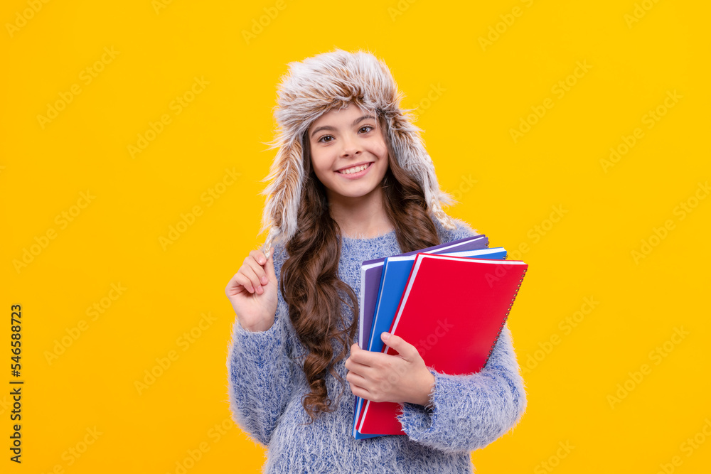 Poster happy teen girl wear earflap hat with notebook on yellow background, education