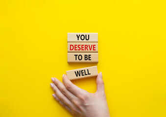 You deserve to be well symbol. Wooden blocks with words You deserve to be well. Beautiful yellow background. Businessman hand. You deserve to be well concept. Copy space.