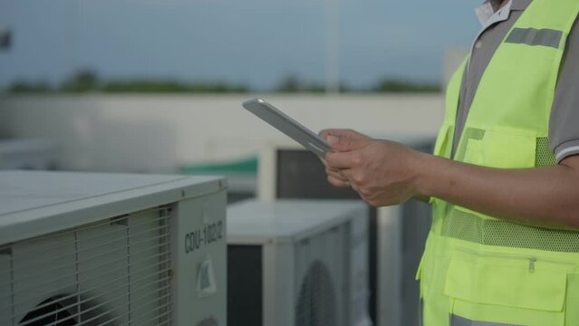 Asian maintenance engineer works on the roof of factory. Supervisor inspect compressor system and plans installation of air condition systems in construction site of modern buildings.