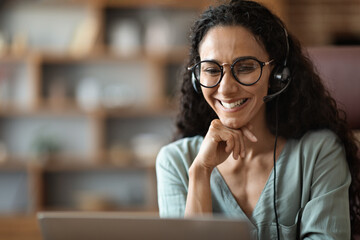 Closeup of eastern woman attending webinar, using computer and headset