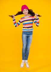 Amazed teenager. Modern teenage girl 12, 13, 14 year old wearing sweater and knitted hat on isolated yellow background. Jump and run. Excited teen girl.