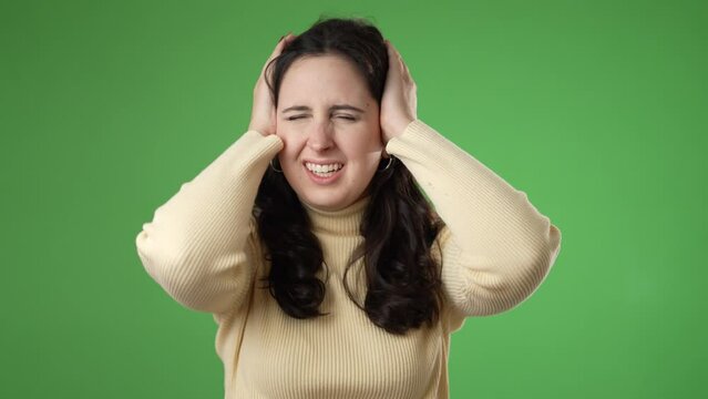 Displeased irritated frustrated sad angry young brunette woman 20s years closed eyes cover ears do not want to listen scream isolated on green screen background studio portrait
