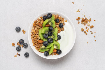 Granola with oatmeal, hazelnuts, kiwis, blueberries and yogurt in white bowl on light background. Morning healthy fast homemade breakfast concept