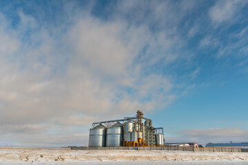 Silver silos against the blue sky in winter. Grain storage in winter at low temperatures. A wheat field covered with snow, the death of a grain crop. Factory for processing, storage of agricultural © Pokoman