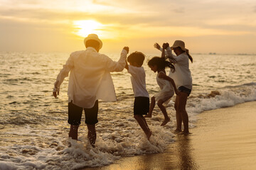 Happy asian family jumping together on the beach in holiday vacation. Silhouette of the family holding hands enjoying the sunset on the sea beach. Happy family travel, trip  family holidays weekend.