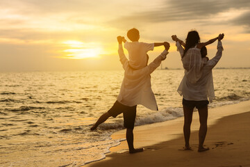 Fototapeta premium Happy asian family on the beach in holiday. of the family holding hands, Son and daughter piggyback on parents.They are having fun playing enjoying the sunset on the beach. Summer Family and lifestyle