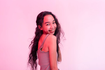 A happy and lively young asian woman posing behind a plain background with hot pink neon effect.
