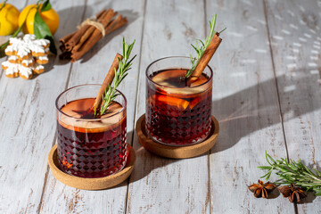 Mulled wine in glasses on white wooden table. Hot winter drink with wine, spices and fruit in...