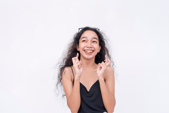 An optimistic asian woman crosses her fingers while looking up, certain about her good luck. Isolated on a white background.