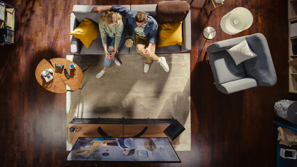Top View Apartment: Happy Couple Watching Television in the Stylish Living Room. Looking at the TV...