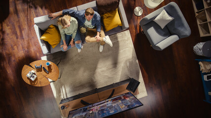 Top View of Apartment: Lovely Couple Watching Television in the Stylish Living Room. Looking at the TV Display and Eating Popcorn. Girlfriend and Boyfriend Watch Sitcom on Streaming Service on Couch.