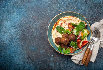 Middle Eastern Arab meal with fried falafel, hummus, vegetables salad with fresh green cilantro and mint leaves in ceramic bowl on stone rustic background top view. Arabic cuisine, space for text