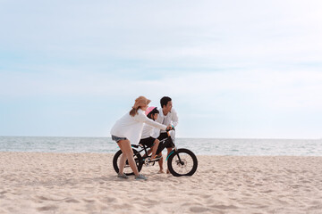 Fototapeta premium Family on the beach they are enjoy bicycle. Happy father, mother and son, daughter enjoying road trip the summer holidays.Parents and children are riding on a bicycle with a sea travel trip exercise