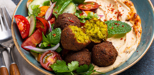 Close up of Middle Eastern Arab meal with fried falafel, hummus, vegetables salad with fresh green cilantro and mint leaves on ceramic plate on stone rustic background table. Arabic traditional cuisin © somegirl