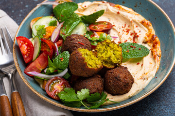 Close up of Middle Eastern Arab meal with fried falafel, hummus, vegetables salad with fresh green cilantro and mint leaves on ceramic plate on stone rustic background table. Arabic traditional cuisin