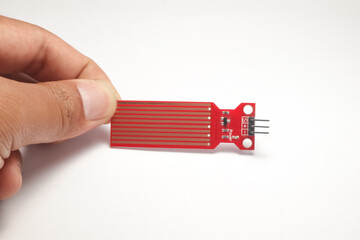A water sensor or red rain sensor is held in a hand which is used as a DIY material for electronics hobbyists