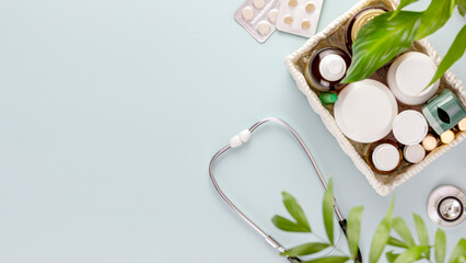 Set of medications with a stethoscope on a blue background with green leaves and copy space. Concept of medicine, healthcare and medication treatment. First aid kit, medicine box. Flat lay