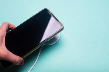 Woman hand plugging a charger in a smartphone. White wireless charging pad and smartphone on the green background.