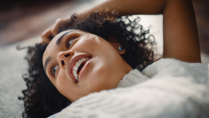 Obraz na płótnie Canvas Close Up Portrait of Black Curly Female Talking with Somebody while Relaxing on the Floor at Home. She Plays with her Hair and Smiles Flirtaciously. Feeling of Falling in Love Concept.