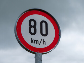 Obraz premium A road sign limiting the speed of 80 km per hour. A road sign against a cloudy sky.