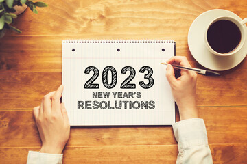 2023 New Years Resolutions with a person holding a pen on a wooden desk