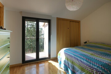 bedroom with a double bed with colored wooden furniture, access to a terrace with black aluminum...