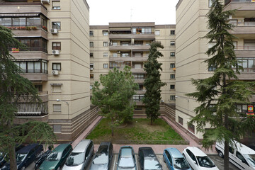 Facades of exposed white brick residential houses with gardens in the middle and many parked cars