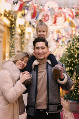 Fototapeta na wymiar happy family mom dad and baby daughter on Christmas fair in big city shopping mall close up photo on illuminated decorations