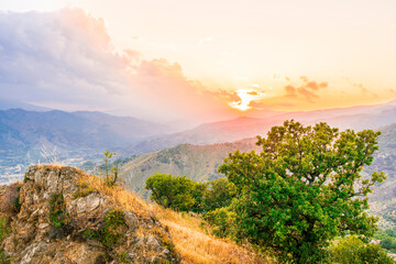 Mountain green mountain side during sunset or sunrise. Natural spring or summer season landscape with trees, branches and cloudy sunset