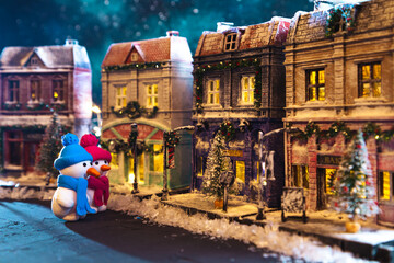 Snowmen on a nightly snow-covered street decorated for Christmas. Homemade decorated toy houses.
