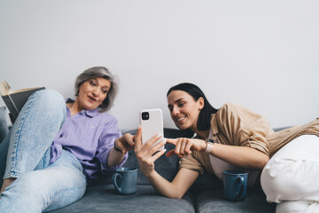 Cheerful mother and daughter with smartphone while sitting on sofa