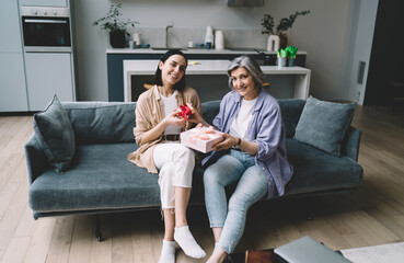 Happy mother and daughter exchanging presents while sitting on sofa