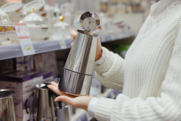 Young woman choosing coffee pot at utensil dishes department in supermarket shop