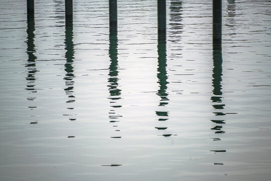 Black mooring piles or dolphins with reflection in the water in an empty yacht marina on the Baltic Sea on a gray November day, abstract image, nearly monochrome, copy space