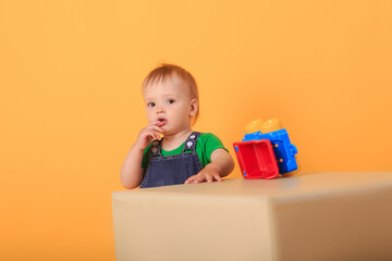 A little handsome boy plays with a toy on a light-colored pouffe . Studio shot of a baby boy against a yellow background.