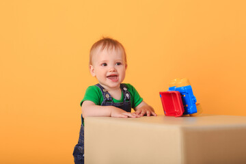 A little handsome boy plays with a toy on a light-colored pouffe . Studio shot of a baby boy against a yellow background.