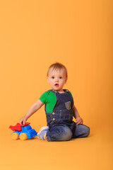 A little boy plays with a toy car. Studio shot of a child playing with a toy against a yellow background.