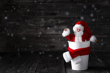 Santa Claus toy in Coffee cup with scarf on wooden background