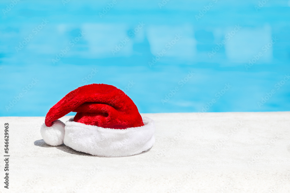 Wall mural Santa Claus hat near swimming pool with clean turquoise water. Christmas celebration at poolside