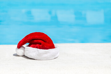 Santa Claus hat near swimming pool with clean turquoise water. Christmas celebration at poolside