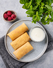 Crepes with raspberry and sour cream on a plate on a light background with fresh mint close up.
