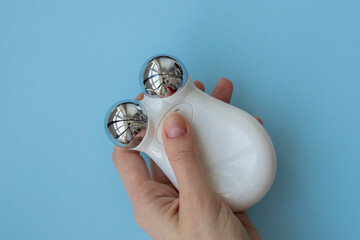 Microcurrent device in the hand on a blue background. Modern cosmetic treatment