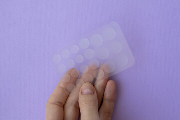 Pimple patch for oily skin in a female hand on a lilac background.