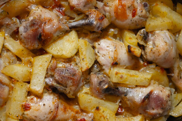 Baked hot potatoes with chicken legs only from the oven. A dish cooked at home. Hot fat and juice heats up, squirts and bubbles on a baking sheet