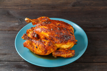 Whole baked chicken carcass stuffed with pears in soy sauce with a crispy crust on a blue plate.