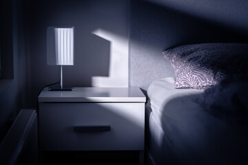 Moonlight in bedroom at night from window. Bed and table in dark room at dusk. Interior design in...
