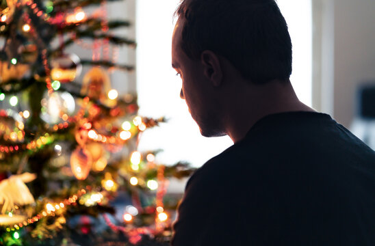 Lonely christmas with sad family conflict or grief on holiday. Man with stress, money problem or depression on Xmas. Unhappy tired person with loneliness in front of a decoration tree at winter home.